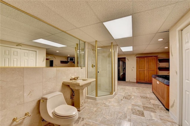 bathroom featuring toilet, a shower with shower door, tile walls, and a drop ceiling