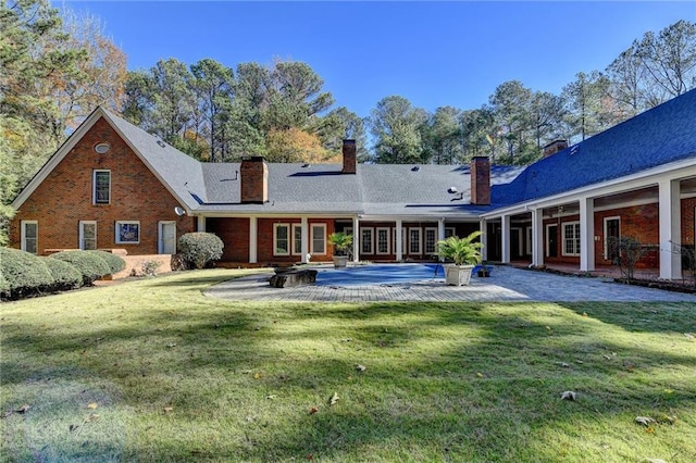 back of house featuring a lawn, a patio area, and a fire pit