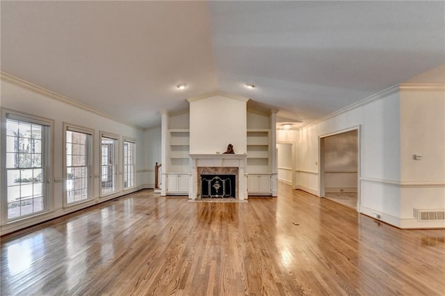 unfurnished living room with lofted ceiling, crown molding, built in shelves, light wood-type flooring, and a premium fireplace