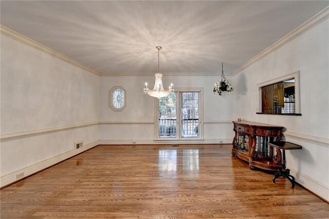 unfurnished dining area with an inviting chandelier, wood-type flooring, and ornamental molding