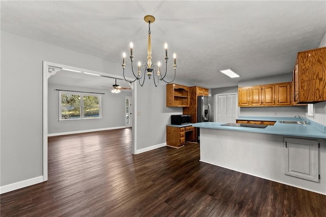 kitchen with dark wood-type flooring, kitchen peninsula, decorative light fixtures, ceiling fan with notable chandelier, and sink