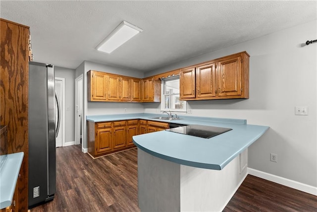 kitchen with kitchen peninsula, dark wood-type flooring, stainless steel fridge, black electric stovetop, and sink