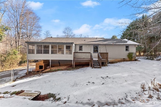 snow covered back of property with a sunroom and a wooden deck