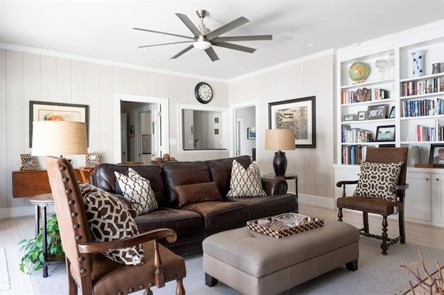 living area featuring built in shelves, light wood-style flooring, a ceiling fan, and crown molding