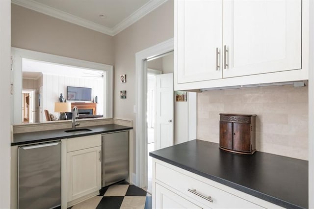 kitchen featuring dark countertops, backsplash, crown molding, stainless steel built in fridge, and a sink