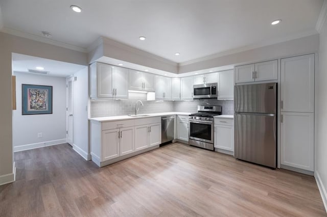 kitchen featuring ornamental molding, a sink, appliances with stainless steel finishes, light wood finished floors, and light countertops