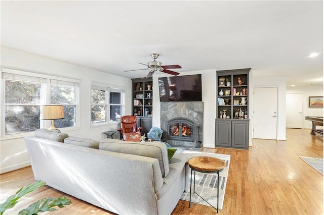 living room with ceiling fan, built in features, and light hardwood / wood-style flooring