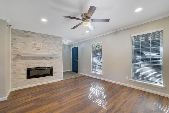 unfurnished living room featuring ceiling fan, dark hardwood / wood-style flooring, a stone fireplace, and ornamental molding