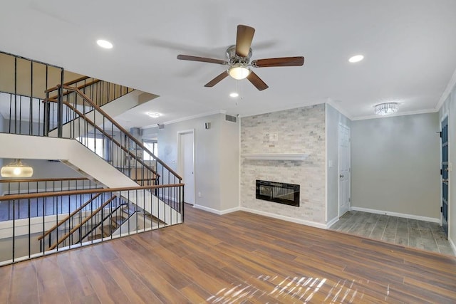 unfurnished living room featuring ceiling fan, a large fireplace, hardwood / wood-style flooring, and crown molding