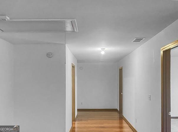 corridor with attic access, light wood-style flooring, baseboards, and visible vents