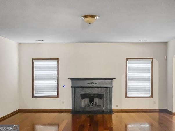 unfurnished living room featuring a fireplace with flush hearth, wood finished floors, baseboards, and a wealth of natural light