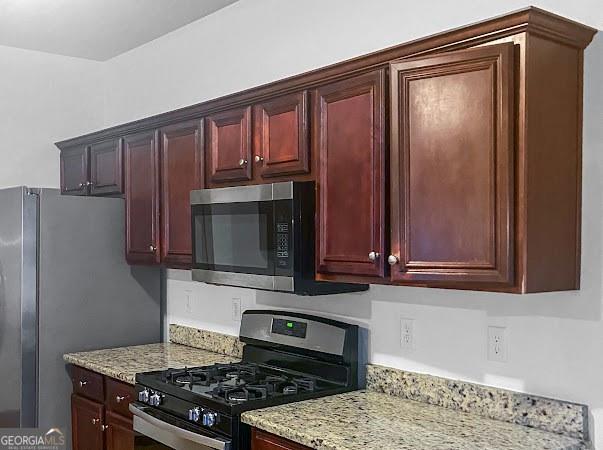 kitchen featuring appliances with stainless steel finishes, light stone countertops, and reddish brown cabinets