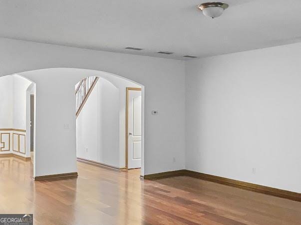 empty room featuring visible vents, wood finished floors, arched walkways, and baseboards