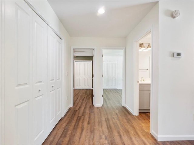 hallway with a sink, wood finished floors, and baseboards