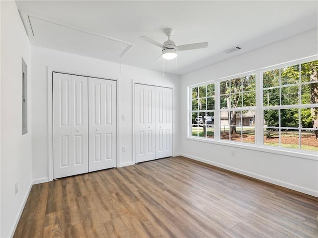 unfurnished bedroom with wood finished floors, visible vents, baseboards, two closets, and attic access