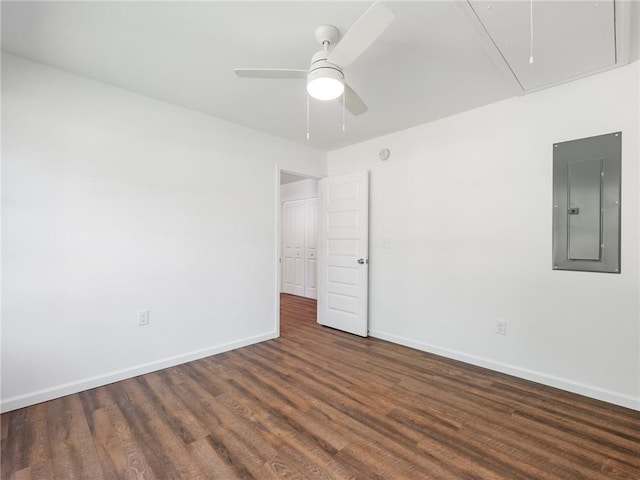 empty room featuring attic access, electric panel, baseboards, a ceiling fan, and wood finished floors