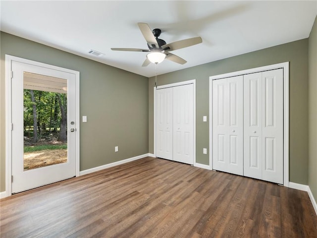 unfurnished bedroom featuring baseboards, visible vents, a ceiling fan, wood finished floors, and two closets