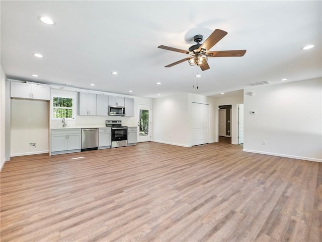 unfurnished living room featuring visible vents, baseboards, light wood-style floors, a sink, and recessed lighting