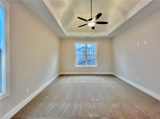 carpeted empty room with a raised ceiling and ceiling fan