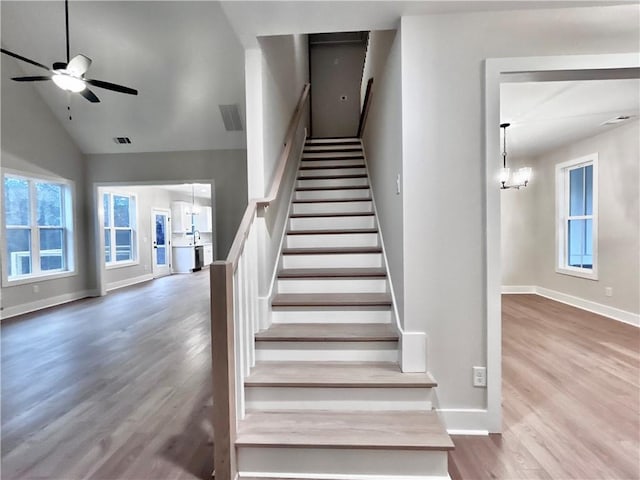 stairway featuring lofted ceiling, ceiling fan with notable chandelier, and wood-type flooring