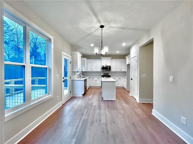 kitchen featuring sink, white cabinetry, decorative light fixtures, light wood-type flooring, and stainless steel appliances