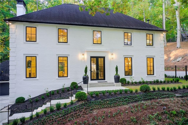 view of front of property with fence, a chimney, entry steps, french doors, and brick siding