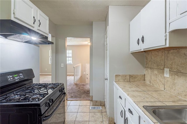 2242 Cherokee Valley Cir, Lithonia, GA 30058 - kitchen with black gas stove, under cabinet range hood, tile countertops, white cabinetry, and tasteful backsplash