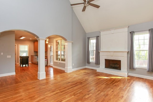 unfurnished living room with ornate columns, high vaulted ceiling, ceiling fan, a brick fireplace, and light hardwood / wood-style flooring