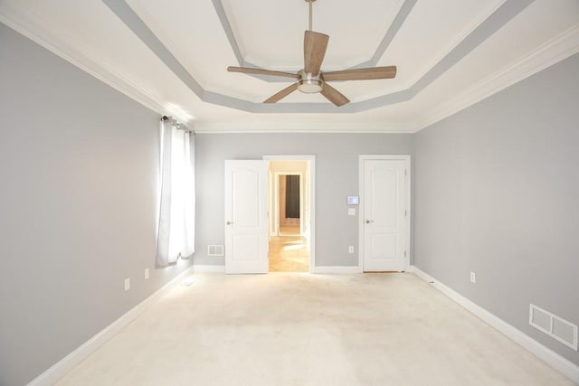 unfurnished room with ceiling fan, light colored carpet, ornamental molding, and a tray ceiling