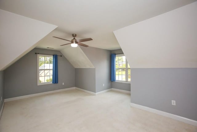 additional living space with vaulted ceiling, a wealth of natural light, light colored carpet, and ceiling fan