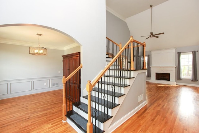 staircase featuring crown molding, wood-type flooring, a high ceiling, and ceiling fan with notable chandelier