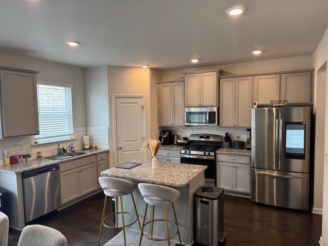 kitchen with a kitchen island, appliances with stainless steel finishes, sink, a kitchen breakfast bar, and light stone countertops