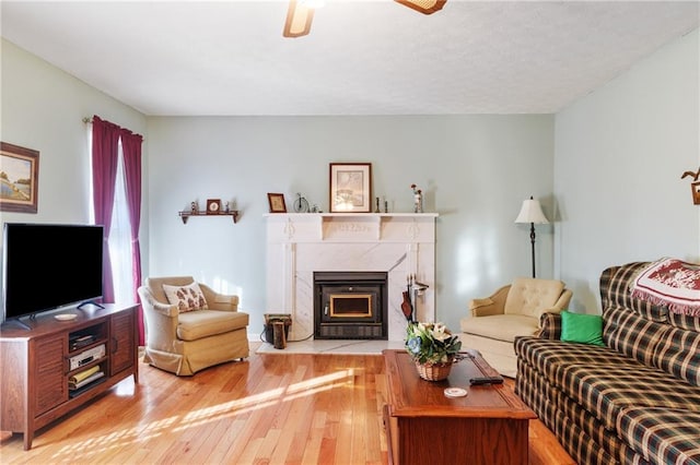 living area with light wood finished floors, a fireplace, and a ceiling fan