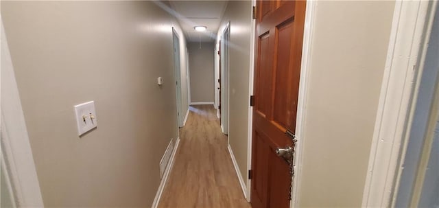 hallway with attic access, light wood-type flooring, and baseboards