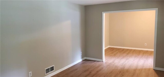 spare room with light wood finished floors, visible vents, and baseboards