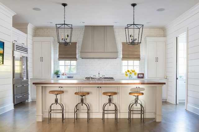 kitchen featuring premium range hood, appliances with stainless steel finishes, a kitchen island with sink, and a breakfast bar