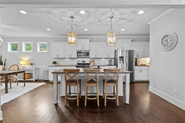 kitchen featuring appliances with stainless steel finishes, crown molding, a kitchen breakfast bar, tasteful backsplash, and an island with sink