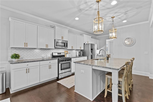 kitchen with stainless steel appliances, a sink, an island with sink, white cabinetry, and crown molding