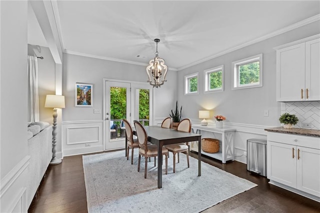dining room featuring ornamental molding, a chandelier, a wainscoted wall, dark wood-style floors, and a decorative wall