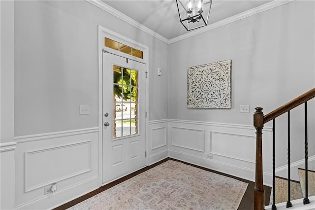 foyer featuring stairway, wainscoting, crown molding, a chandelier, and wood finished floors