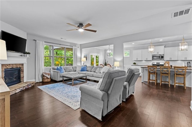 living room featuring a ceiling fan, dark wood-style flooring, and a stone fireplace