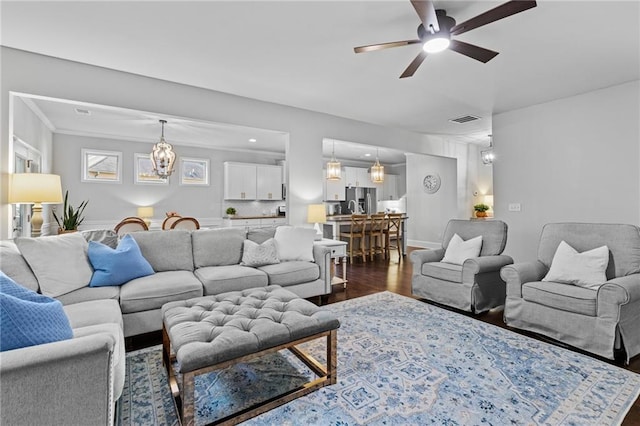 living area featuring dark wood-type flooring, a ceiling fan, a chandelier, recessed lighting, and crown molding