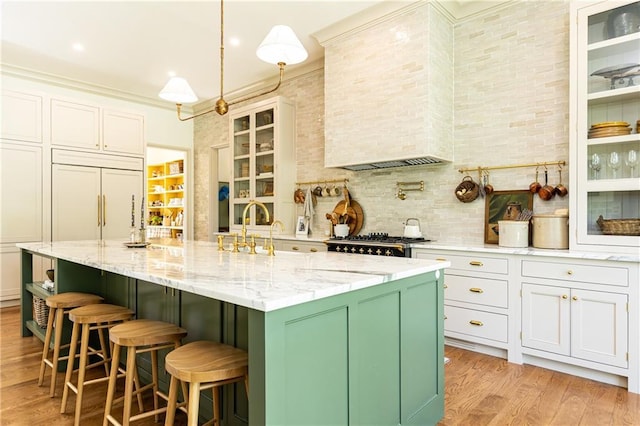 kitchen featuring light stone counters, a sink, an island with sink, paneled built in refrigerator, and light wood-type flooring