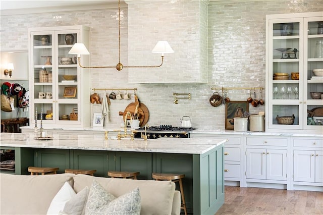 kitchen with glass insert cabinets, light wood finished floors, a kitchen bar, and light stone countertops