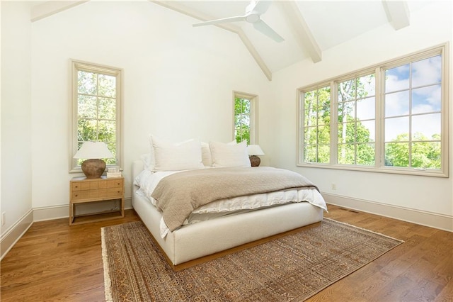 bedroom featuring baseboards, multiple windows, lofted ceiling with beams, and wood finished floors