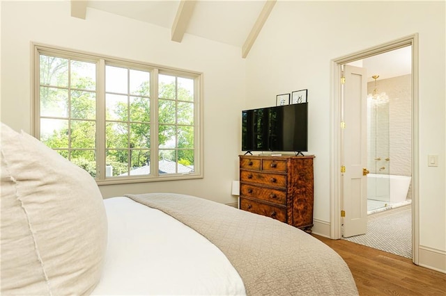 bedroom featuring vaulted ceiling with beams, ensuite bath, and wood finished floors
