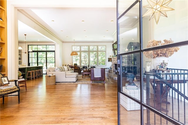 living area featuring light wood-style floors, crown molding, and a healthy amount of sunlight