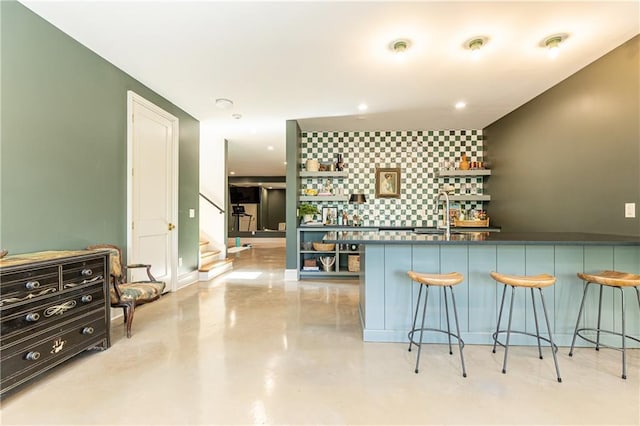 kitchen featuring concrete flooring, open shelves, a breakfast bar, a sink, and recessed lighting