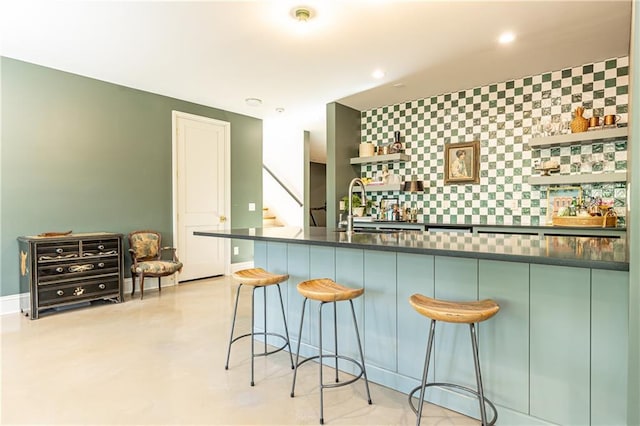 kitchen with open shelves, a breakfast bar, dark countertops, a sink, and an accent wall
