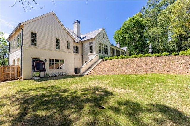 back of property featuring fence, a chimney, a lawn, and stairway
